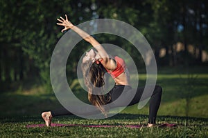 Young woman doing yoga exercises in the summer city park. Health lifestyle concept.