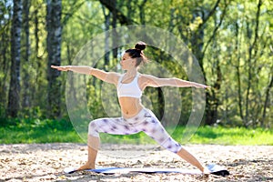 Young woman doing yoga exercises in the summer city park. Health lifestyle concept.