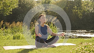 Young woman doing yoga exercises in summer city park. Health lifestyle concept. Portrait of peaceful female meditating in the morn