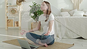 Young woman doing yoga exercises using laptop while sitting on floor at home