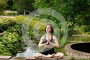 Young woman doing yoga. Girl sitting in the lotus position in the park near a small decorative lake