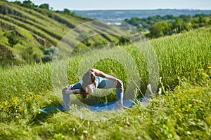 Young woman doing yoga in green summer meadow