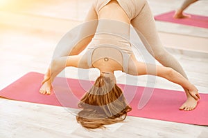 Young woman doing yoga in the gym. A girl with long hair and in a beige tracksuit stands in the Prasarita Padottanasana