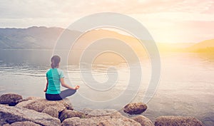 Young woman doing yoga in Lotus pose in the mountain and sunrise background