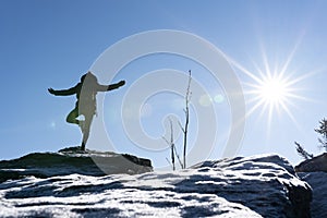 Young woman is doing yoga on a mountain peak with ice in the foreground. Bavarian forest, osser, germany.