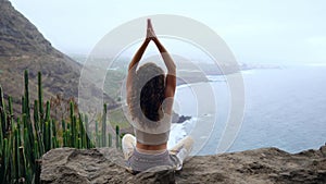 Young woman doing yoga in the mountains on an island overlooking the ocean sitting on a rock on top of a mountain