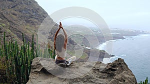 Young woman doing yoga in the mountains on an island overlooking the ocean sitting on a rock on top of a mountain