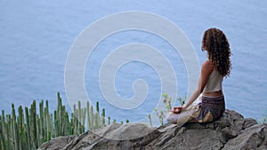 Young woman doing yoga in the mountains on an island overlooking the ocean sitting on a rock on top of a mountain