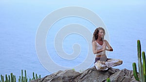 Young woman doing yoga in the mountains on an island overlooking the ocean sitting on a rock on top of a mountain