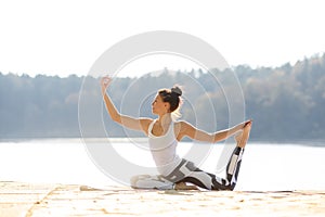 Young woman doing yoga near lake outdoors, meditation. Sport fitness and exercising in nature. Autumn sunset.