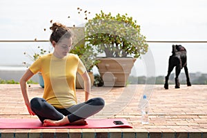 Young woman doing yoga outdoor with dog on background