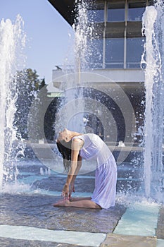 young woman doing yoga pose in city fountain