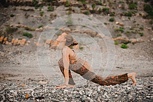 Young woman doing yoga on a rocky seashore. upward facing dog pose