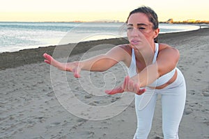 Young woman is doing yoga on the sandy beach at sunrise.