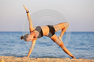 Young woman doing yoga side plank pose or vasistasana at the beach