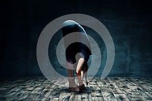 Young woman doing yoga standing forward bend pose in dark room