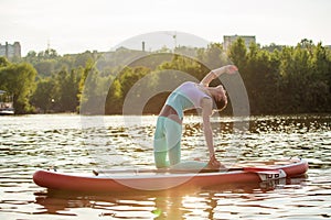 Young woman doing yoga on sup board with paddle. Yoga pose, side view - concept of harmony with the nature.