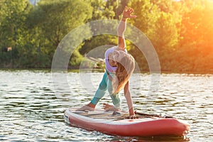 Young woman doing yoga on sup board with paddle. Yoga pose, side view - concept of harmony with the nature.