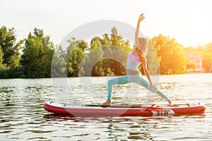 Young woman doing yoga on sup board with paddle. Yoga pose, side view - concept of harmony with the nature.