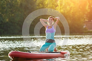 Young woman doing yoga on sup board with paddle. Yoga pose, side view - concept of harmony with the nature.