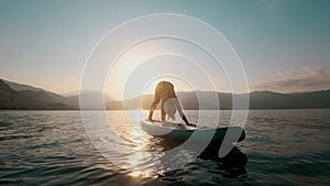 Young woman doing yoga on SUP board at sunset in slow motion