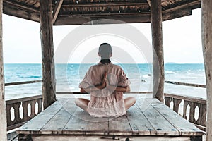 Young woman doing yoga in the wooden gazebo at the beach