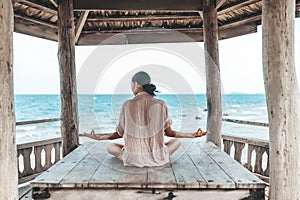 Young woman doing yoga in the wooden gazebo at the beach