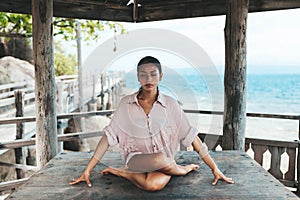 Young woman doing yoga in the wooden gazebo at the beach