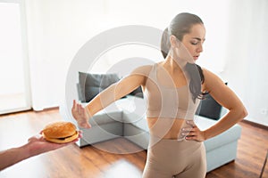 Young woman doing yoga workout in room during quarantine. Girl refuse to eat burger. Say no to unhealthy food.