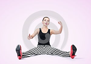 Young woman doll in stripe pants with arms outstretched sitting on the floor fashion style glamor. On light pink background