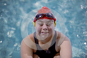 Young woman with Down syndrome swimming in swimming pool and looking at camera