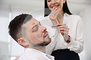 Young woman drawing on colleague`s face while he sleeping in office. Funny joke
