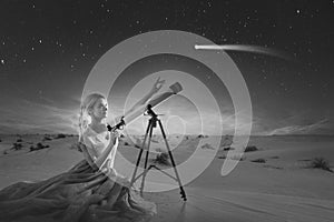 Young woman dreams, concept. Girl looks at a comet or falling star uses a telescope. Desert background,