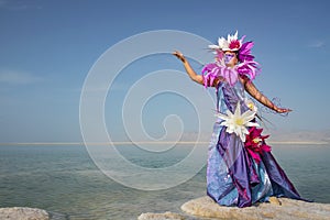 Young woman in a dress decorated with artificial flowers standing on a salty formation