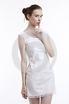 Young woman in dress gesturing to be quiet over white background