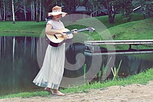 Young woman in dress with a guitar on lake. Country picnic outdoor