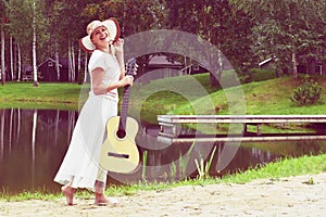 Young woman in dress with a guitar on lake. Country picnic outdoor