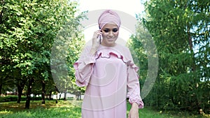 Young woman in dress with hijab talks on black smartphone