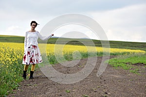 Young woman in dress hitchhiking near a canola field