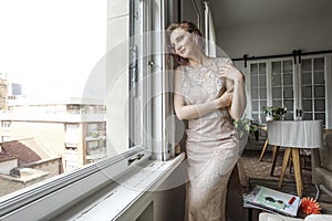 Young woman in dress looking out the window