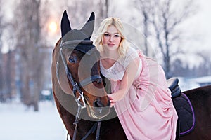 Young woman in dress riding horse on winter field