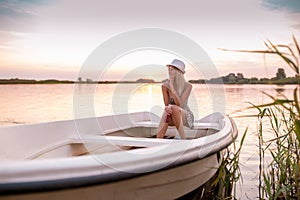 Young woman in a dress sitting on the boat and enjoying in a beautiful sunset while drinking beer