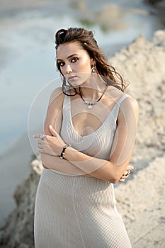 Young woman in dress standing separately on an empty sandy beach near the sea