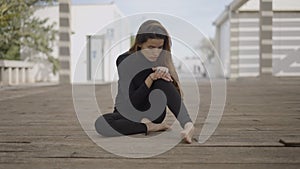 Young woman dressed in black sits outdoors looking shocked, push-in