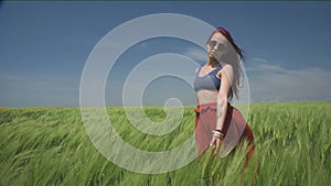 Young woman dressed in Boho style swaying in the middle of green wheat field is catching wind blowing Close her eyes to