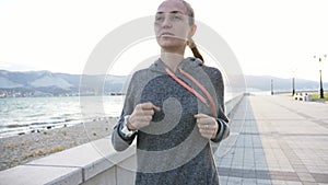 Young woman dressed in hoodie jogging in the city at seafront