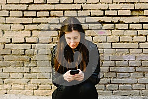 Young woman dressed in leather jacket consulting her phone disappointed in the absence of his appointment, he is late