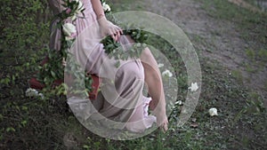 Young woman dressed in light pinc tunic playfully exposing her leg, sitting on decorated with flowers swing