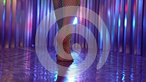 young woman dressed net stockings is walking in room with disco lights, closeup of bare feet, rear view