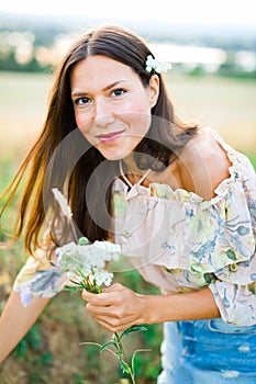 Young woman dressed in summer dress gather meadow flowers